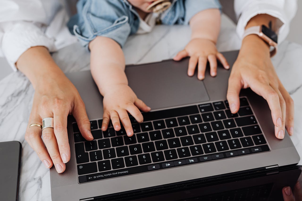 Close-up of mother and child hands on laptop keyboard, symbolizing multitasking and family bonding.